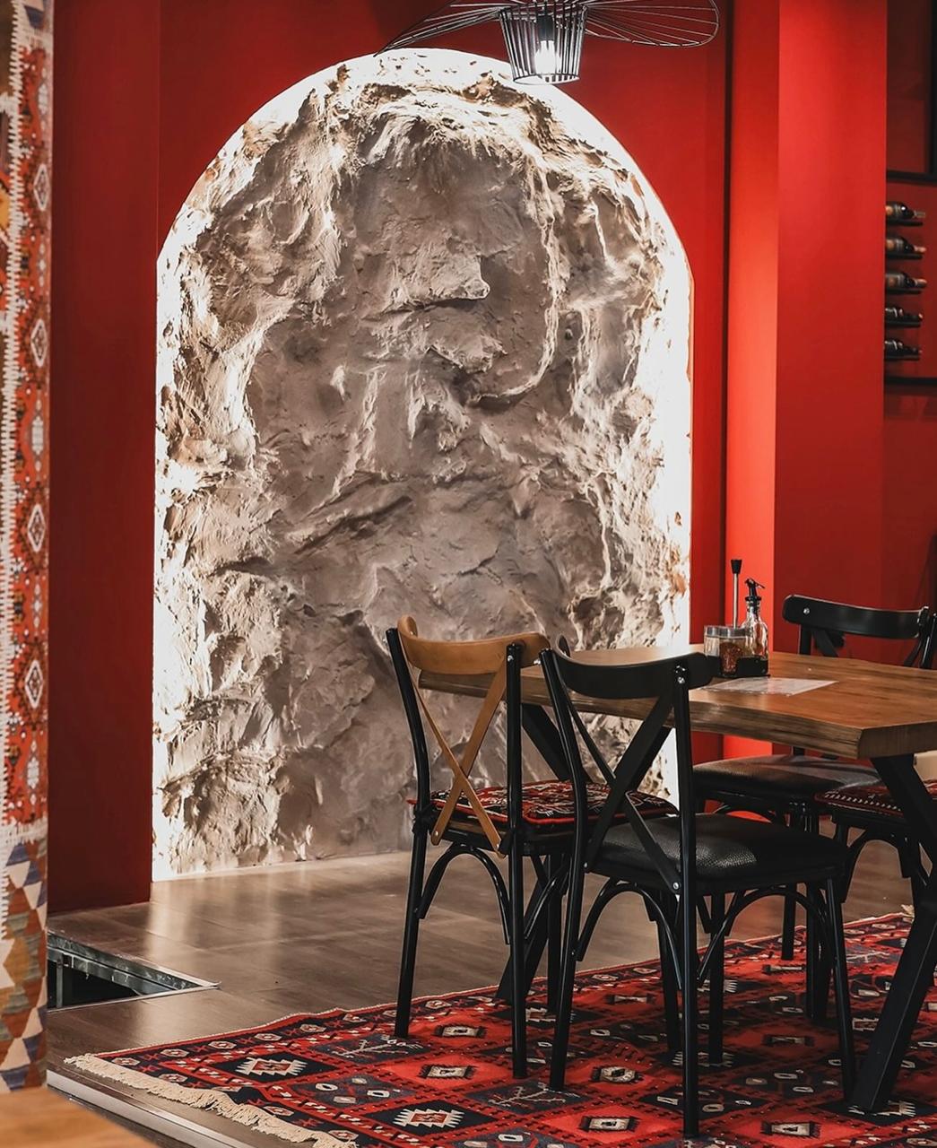 Brendësia e Odës së Prizrenit — Hark guri, mure të kuqe, qilim tradicional shqiptar dhe tavolinë darke